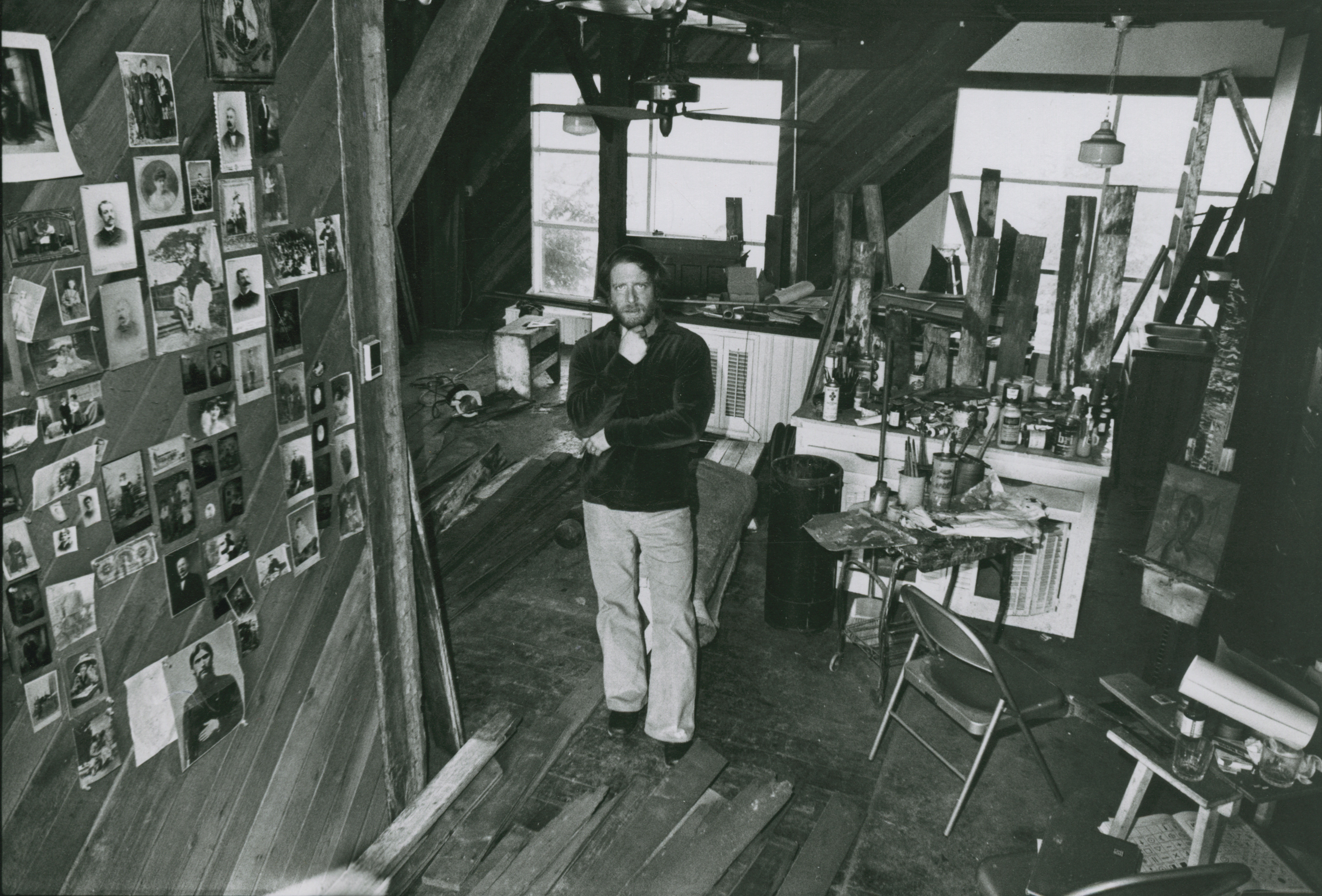 Black and white photo of Gil Stone in his barn like studio, surrounded by artworks
